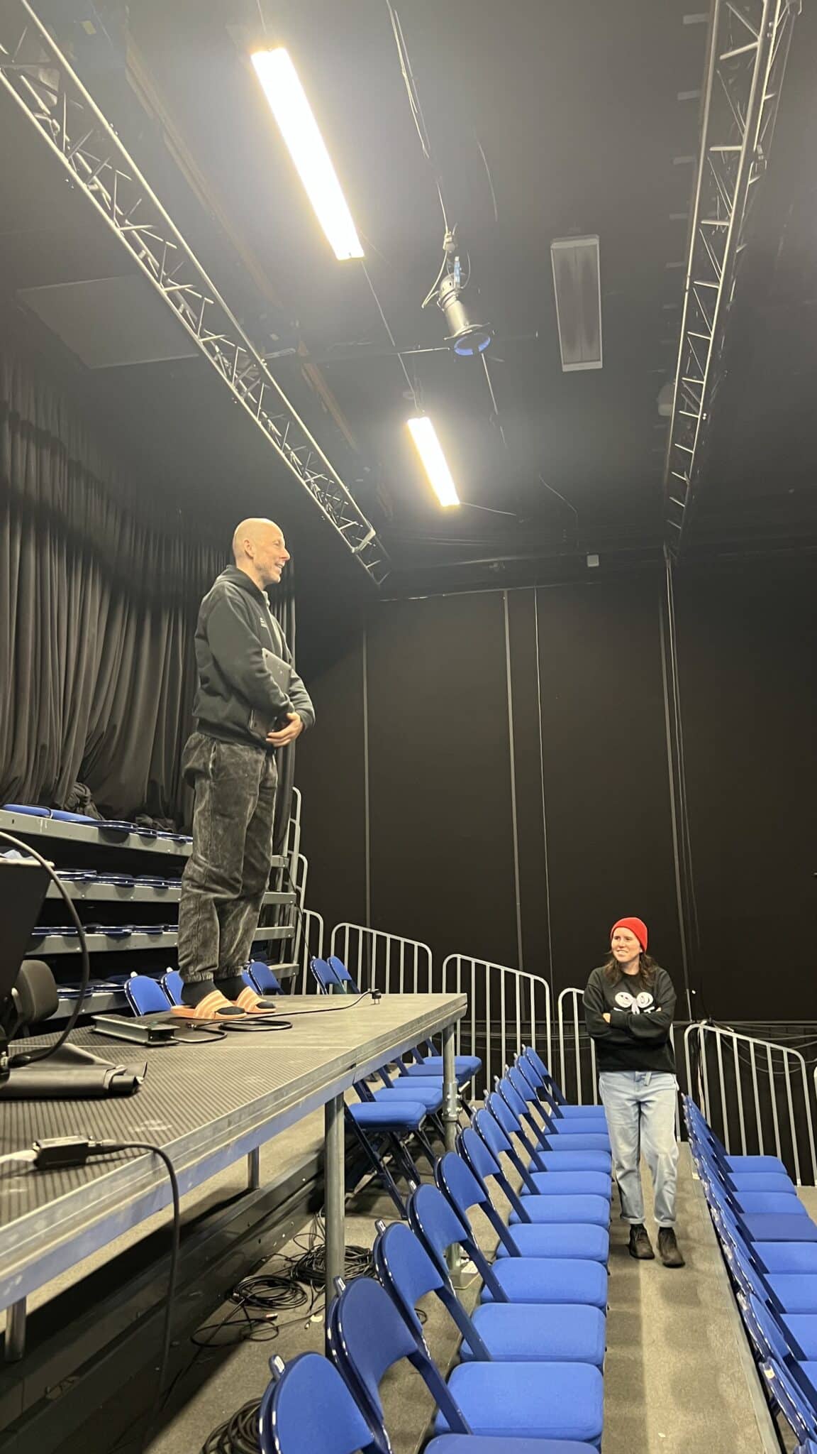 Choreographer Jan Martens standing on the tech table in Studio Bergen; lighting designer Elke Verachtert (red hat) below. Koreograf Jan Martens står på teknikerbordet i Studio Bergen; lysdesigner Elke Verachtert (rød lue) nedenfor.